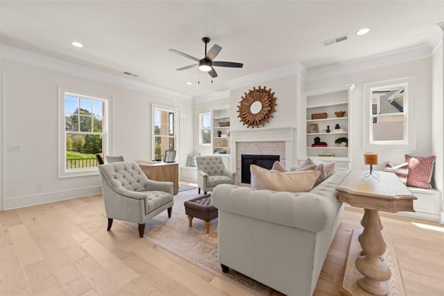 living room with ornamental molding, built in features, a fireplace, and light hardwood / wood-style floors