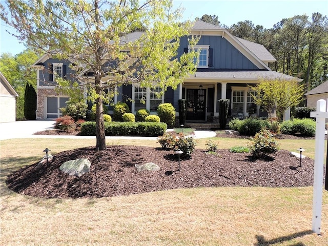 craftsman-style house with board and batten siding, covered porch, a front yard, an attached garage, and driveway
