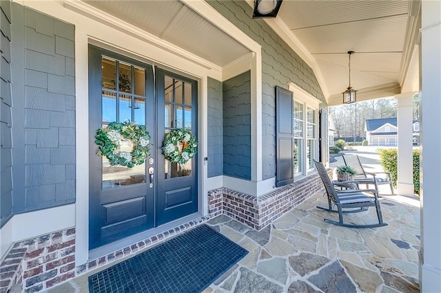 view of exterior entry featuring covered porch, french doors, and brick siding