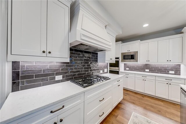 kitchen featuring appliances with stainless steel finishes, custom range hood, white cabinetry, tasteful backsplash, and recessed lighting
