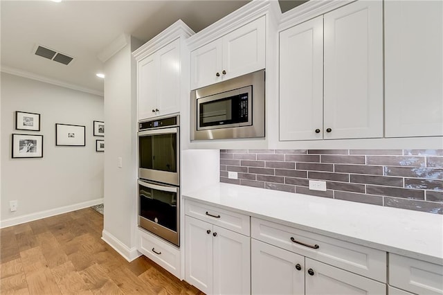 kitchen with stainless steel appliances, light countertops, baseboards, ornamental molding, and white cabinetry