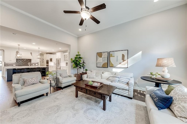 living area with ceiling fan, recessed lighting, ornamental molding, and light wood-style floors
