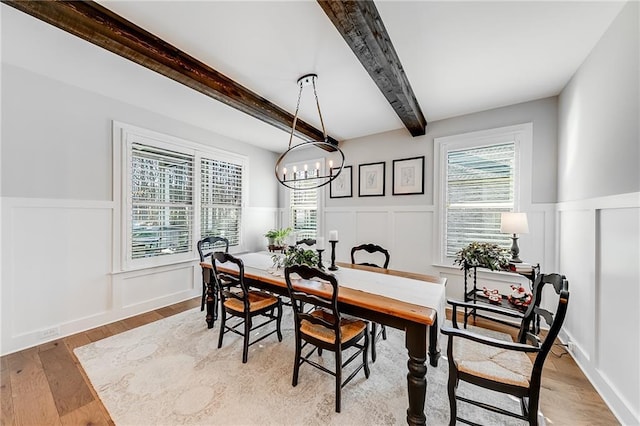 dining space featuring a decorative wall, a wainscoted wall, a chandelier, beamed ceiling, and wood finished floors