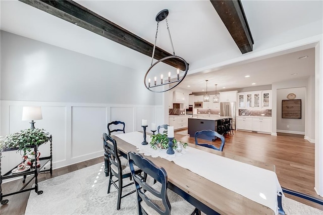 dining room featuring beam ceiling, a chandelier, light wood-style flooring, recessed lighting, and a decorative wall
