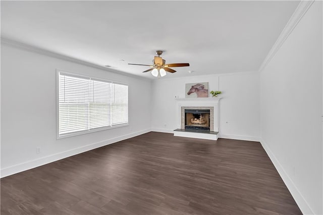 unfurnished living room featuring crown molding, a fireplace with raised hearth, a ceiling fan, dark wood-type flooring, and baseboards