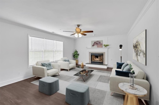 living room featuring crown molding, wood finished floors, a ceiling fan, a fireplace with raised hearth, and baseboards