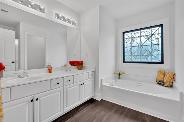 full bath featuring wood finished floors, double vanity, a garden tub, and baseboards