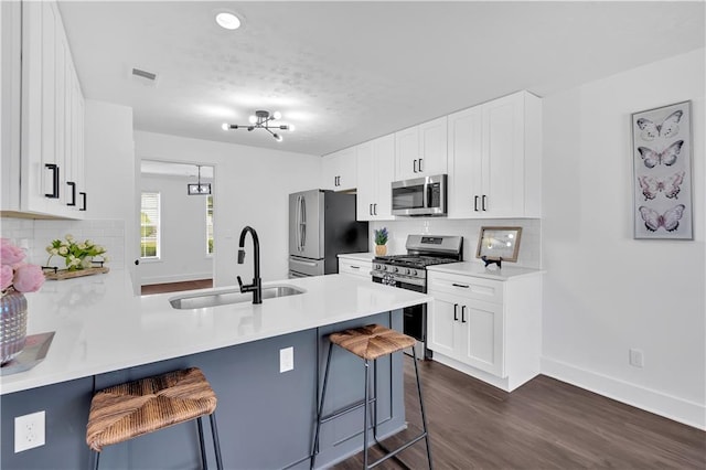 kitchen featuring appliances with stainless steel finishes, a sink, a breakfast bar, a peninsula, and dark wood-type flooring
