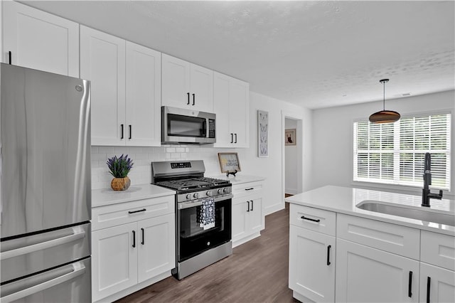 kitchen featuring stainless steel appliances, a sink, light countertops, backsplash, and dark wood-style flooring