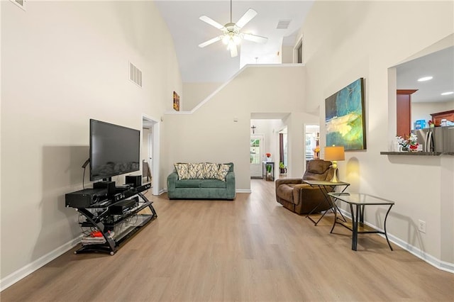 living room featuring ceiling fan, light wood-type flooring, and a towering ceiling