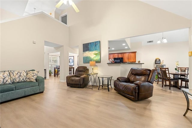 living room with ceiling fan with notable chandelier, light hardwood / wood-style flooring, and high vaulted ceiling