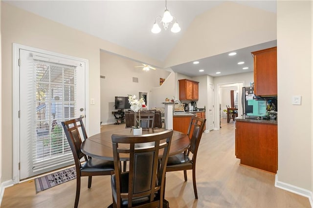 dining area with light wood-type flooring, ceiling fan with notable chandelier, and high vaulted ceiling