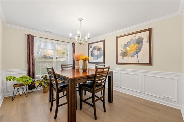 dining space with light wood-type flooring, ornamental molding, and a notable chandelier