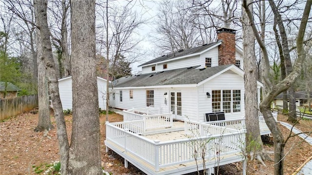 back of property with a chimney, roof with shingles, fence, and a deck