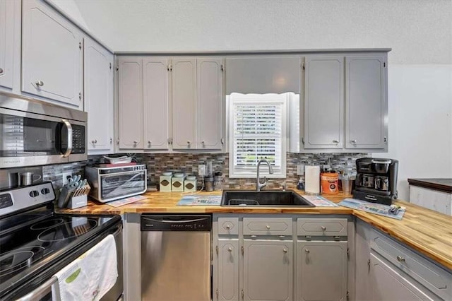 kitchen with gray cabinetry, stainless steel appliances, wood counters, and sink