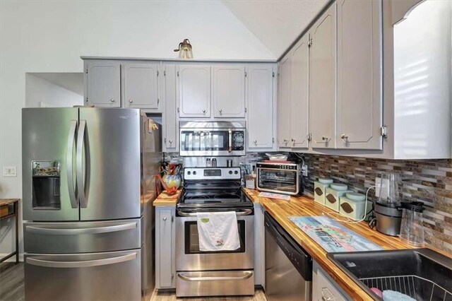 kitchen featuring tasteful backsplash, appliances with stainless steel finishes, butcher block countertops, lofted ceiling, and gray cabinets