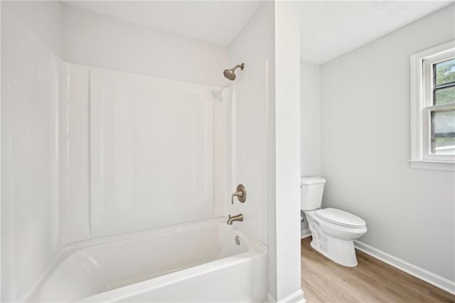 full bath featuring toilet, wood finished floors, a textured ceiling, baseboards, and shower / bathtub combination