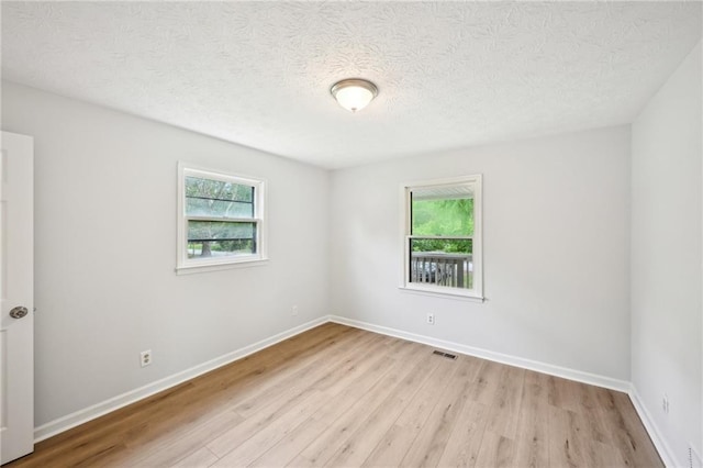 empty room featuring light wood finished floors, a textured ceiling, baseboards, and visible vents