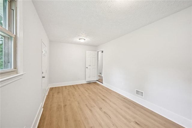 empty room with light wood-style floors, visible vents, baseboards, and a textured ceiling