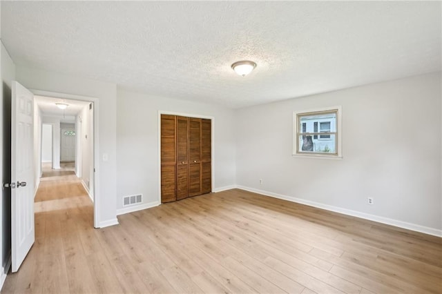 unfurnished bedroom featuring a closet, a textured ceiling, baseboards, visible vents, and light wood-type flooring