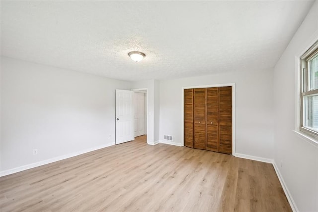 unfurnished bedroom featuring a closet, a textured ceiling, visible vents, baseboards, and light wood-style floors