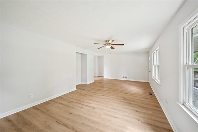 empty room with a ceiling fan, a wealth of natural light, baseboards, and light wood-type flooring