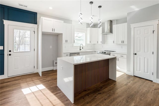 kitchen featuring wall chimney range hood, white cabinetry, stainless steel appliances, a center island, and decorative light fixtures