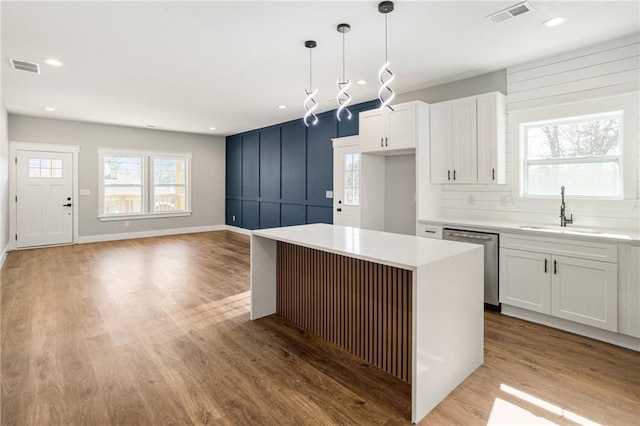 kitchen with white cabinets, light countertops, a sink, and dishwasher