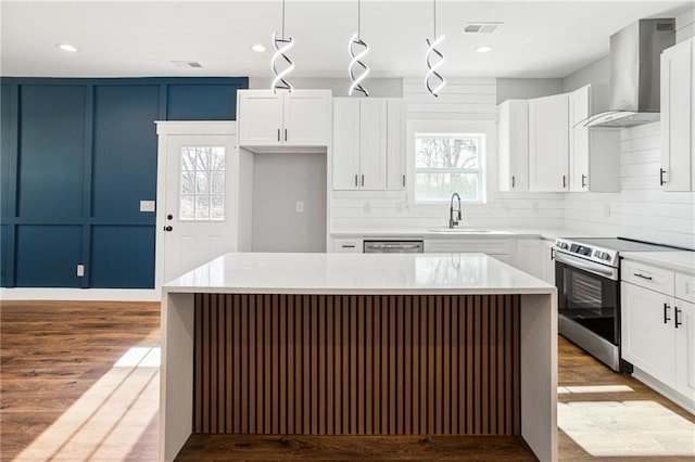 kitchen featuring pendant lighting, stainless steel appliances, wall chimney exhaust hood, and a kitchen island