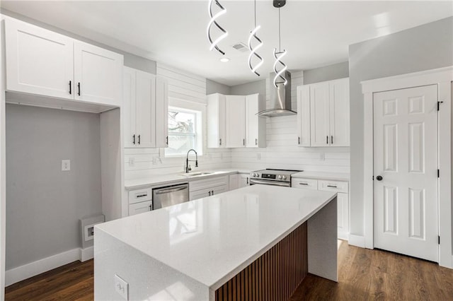 kitchen with stainless steel appliances, light countertops, a kitchen island, wall chimney range hood, and a sink