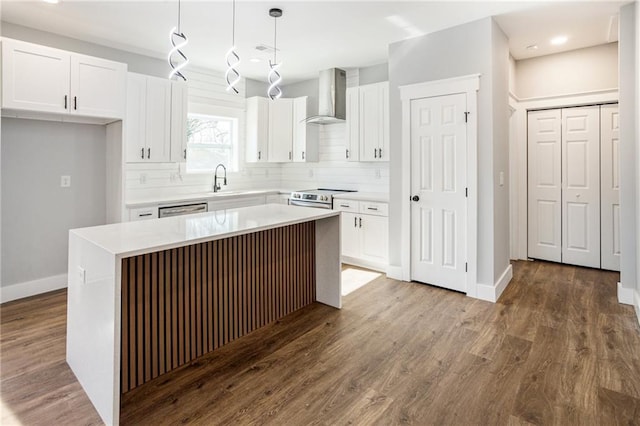 kitchen with appliances with stainless steel finishes, hanging light fixtures, a center island, white cabinets, and wall chimney exhaust hood