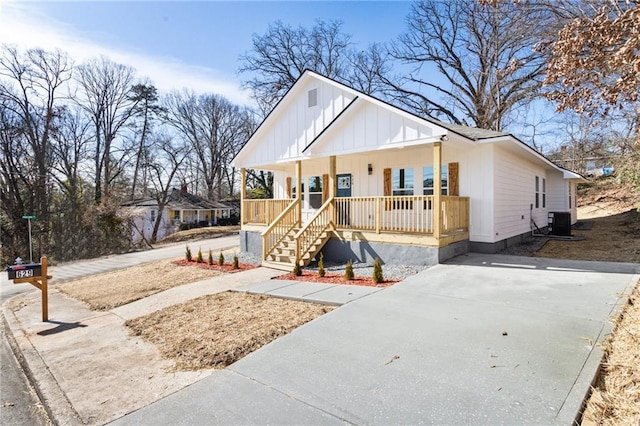 view of front of home with covered porch, driveway, board and batten siding, and cooling unit