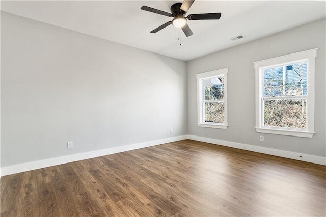 empty room featuring a ceiling fan, visible vents, baseboards, and wood finished floors