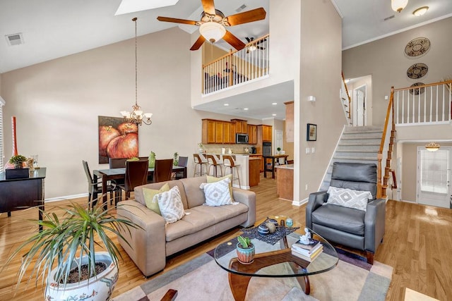 living area featuring high vaulted ceiling, light wood-style flooring, baseboards, and stairs