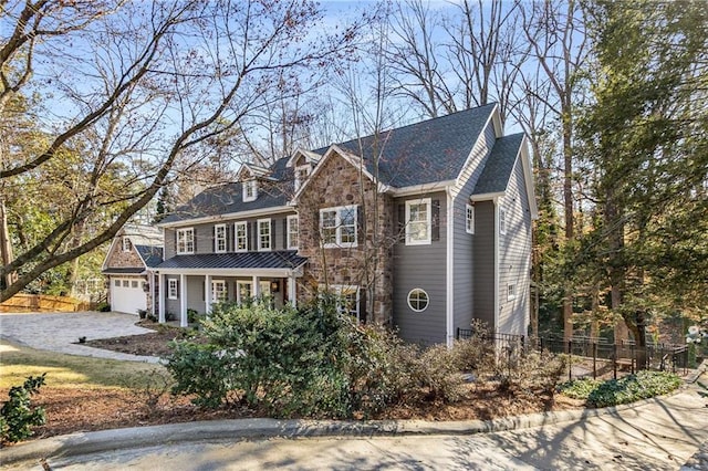 view of front of property featuring stone siding, driveway, an attached garage, and fence