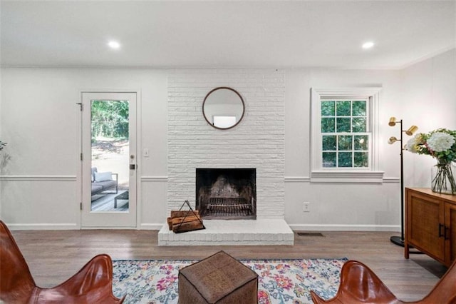 living room featuring ornamental molding, a brick fireplace, light wood-type flooring, and a healthy amount of sunlight