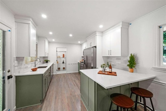 kitchen with stainless steel fridge, hardwood / wood-style floors, a kitchen bar, sink, and green cabinets