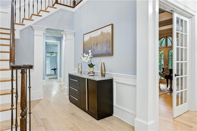 6225 Random Winds Blf, Gainesville, GA 30506 - bar with light wood-style floors, stairway, a wainscoted wall, decorative columns, and french doors
