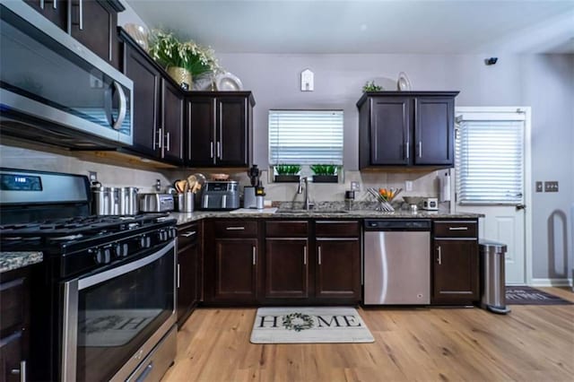 kitchen with dark brown cabinets, dark stone counters, light wood-style floors, stainless steel appliances, and a sink