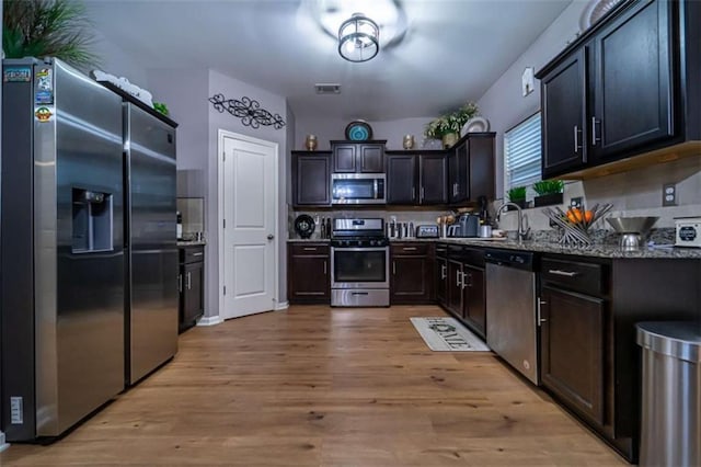 kitchen featuring light wood finished floors, visible vents, stone counters, stainless steel appliances, and a sink