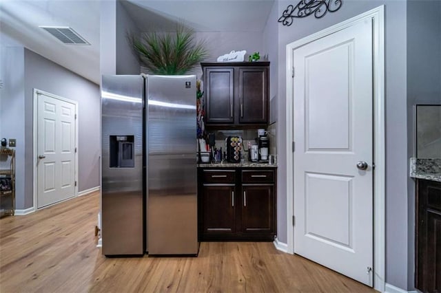 kitchen featuring light wood finished floors, visible vents, stainless steel fridge, and light stone countertops