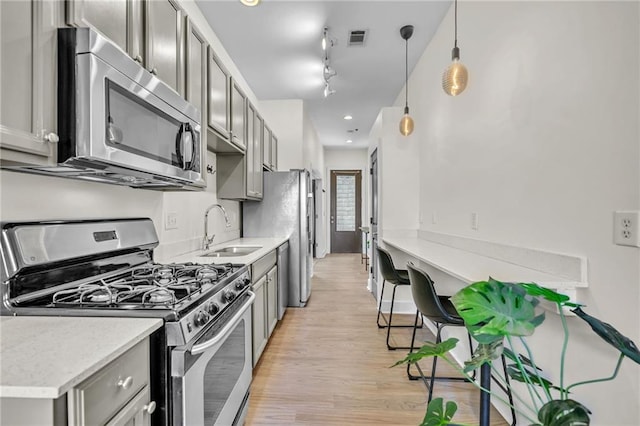 kitchen with appliances with stainless steel finishes, sink, light wood-type flooring, pendant lighting, and gray cabinets