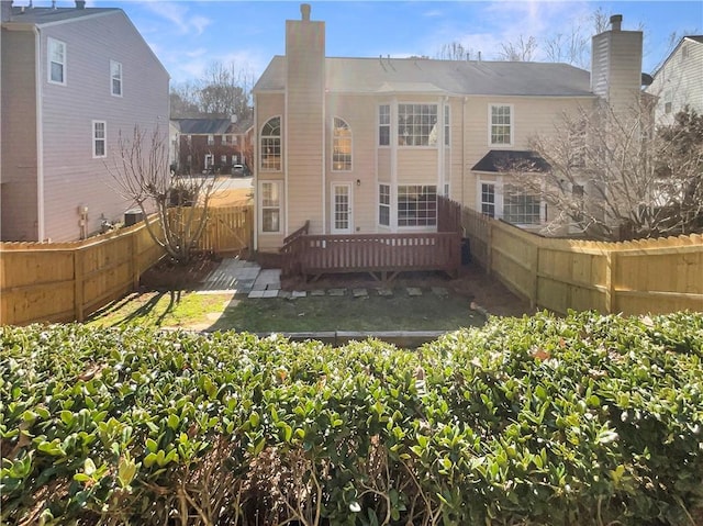 rear view of house with a chimney, a fenced backyard, and a wooden deck