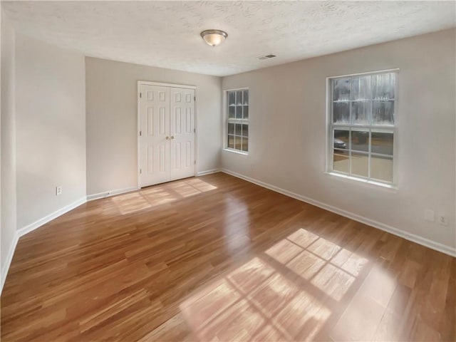 unfurnished bedroom featuring baseboards, visible vents, light wood-style flooring, a textured ceiling, and a closet