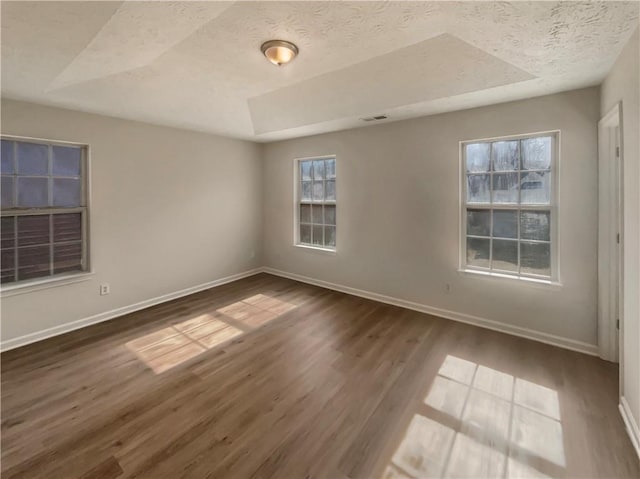 spare room with visible vents, a textured ceiling, baseboards, and wood finished floors