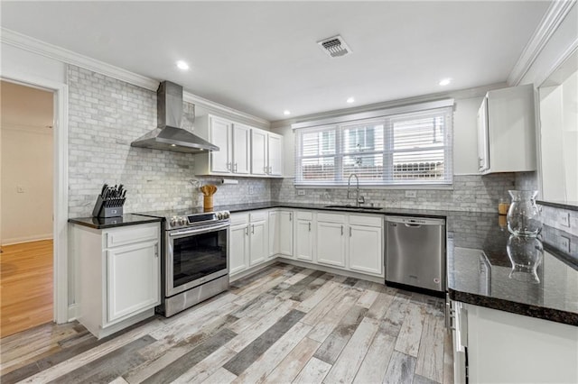 kitchen featuring wall chimney range hood, sink, light hardwood / wood-style flooring, stainless steel appliances, and white cabinets