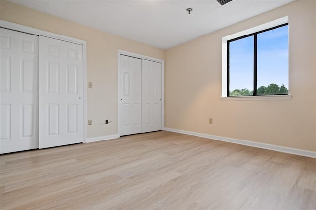 unfurnished bedroom with light wood-type flooring and multiple closets