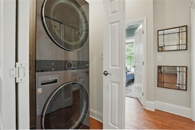 clothes washing area featuring stacked washing machine and dryer, baseboards, and wood finished floors