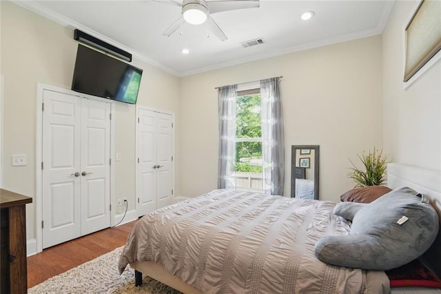 bedroom featuring wood finished floors, ornamental molding, recessed lighting, two closets, and a ceiling fan