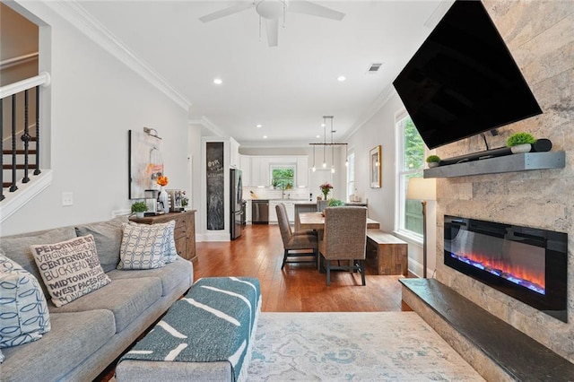 living area with wood finished floors, crown molding, a glass covered fireplace, stairs, and recessed lighting